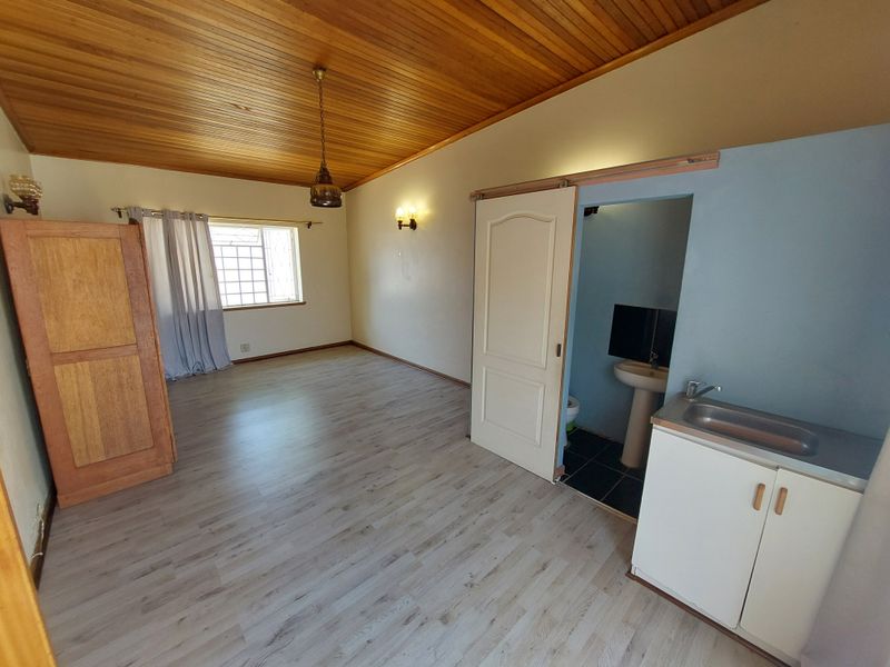 A bedroom featuring a timber ceiling, laminate flooring, and an en-suite bathroom with a pedestal basin and vanity cabinet.