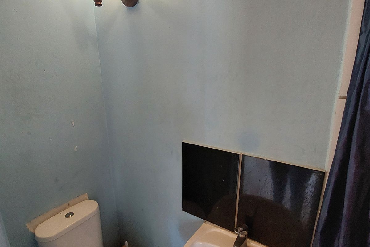A compact bathroom featuring a pedestal basin, toilet, and wall-mounted lighting, requiring cosmetic updates to improve the overall finish and appeal.