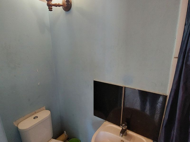 A compact bathroom featuring a pedestal basin, toilet, and wall-mounted lighting, requiring cosmetic updates to improve the overall finish and appeal.