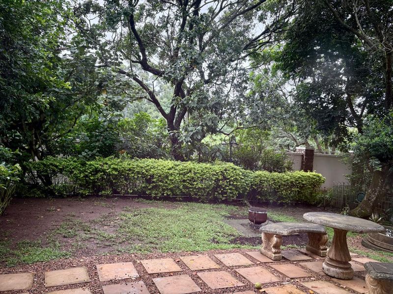 A private garden area featuring a paved patio, established trees, and a boundary wall, offering a quiet outdoor space.
