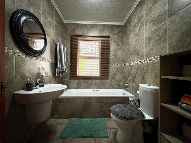 A well-maintained bathroom featuring full-height ceramic wall tiling, a built-in bathtub, a wall-mounted basin, and a toilet.