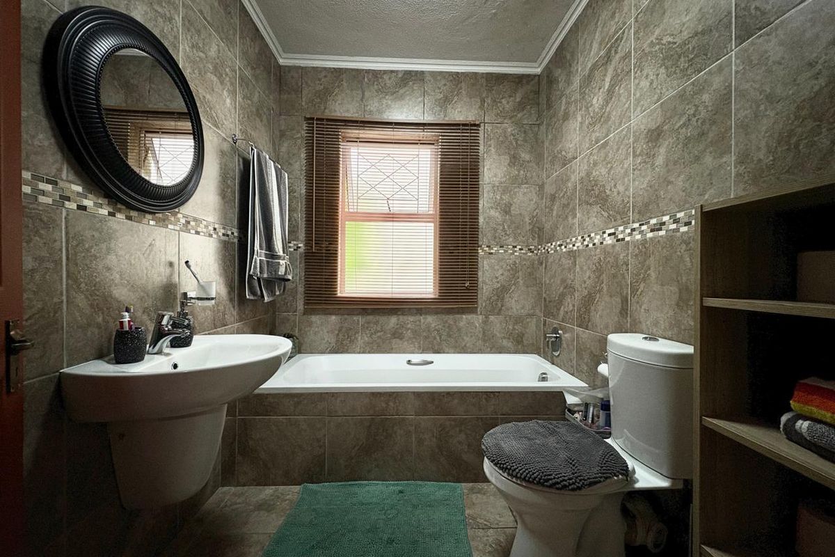 A well-maintained bathroom featuring full-height ceramic wall tiling, a built-in bathtub, a wall-mounted basin, and a toilet.