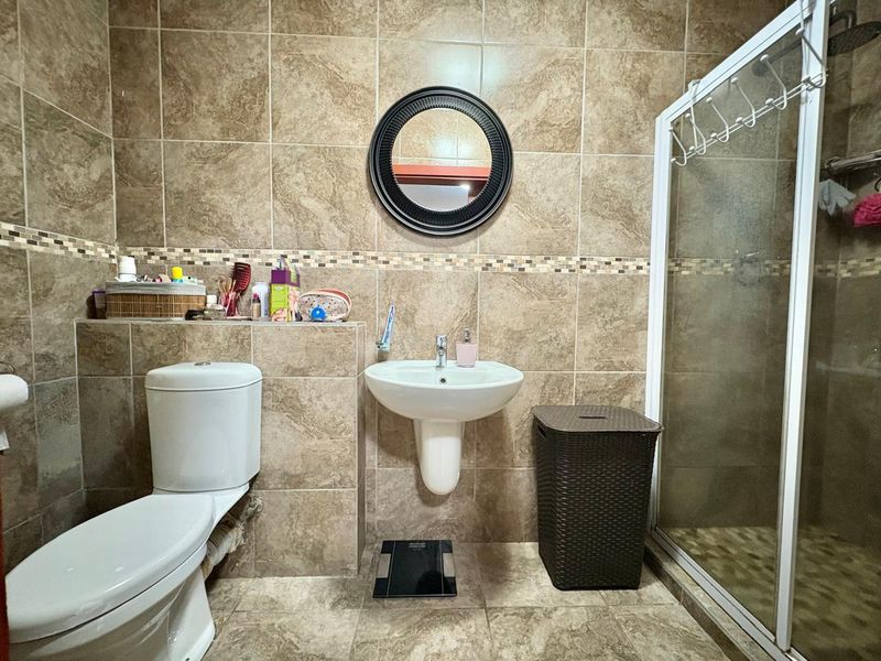 A functional bathroom featuring tiled walls and flooring, a pedestal washbasin, a toilet, and a glass-enclosed shower unit.