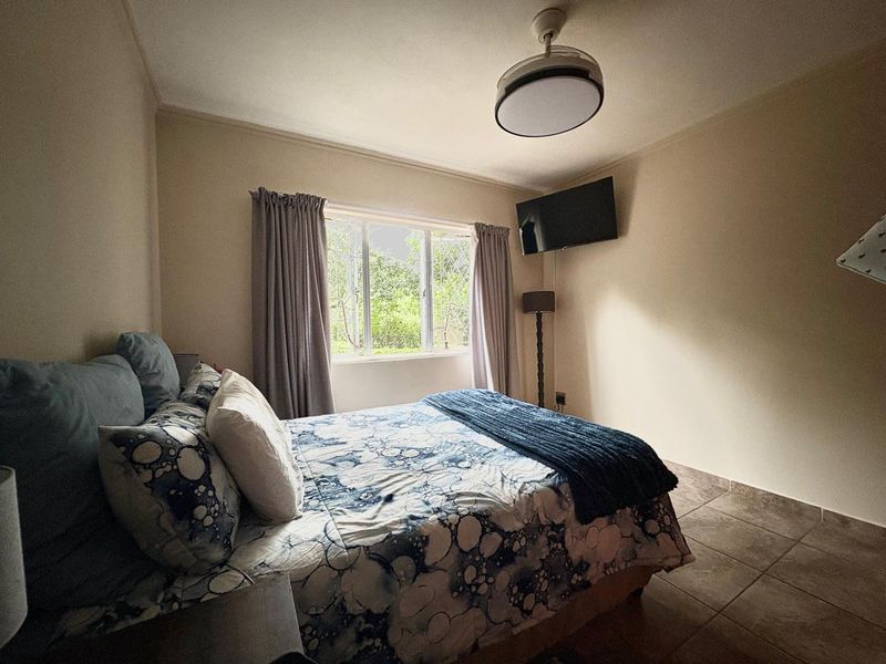 A functional bedroom featuring tiled flooring, a ceiling fan, and security bars on the window, providing a comfortable and secure living space.