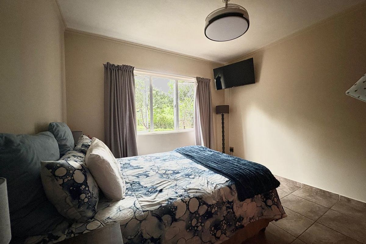 A functional bedroom featuring tiled flooring, a ceiling fan, and security bars on the window, providing a comfortable and secure living space.