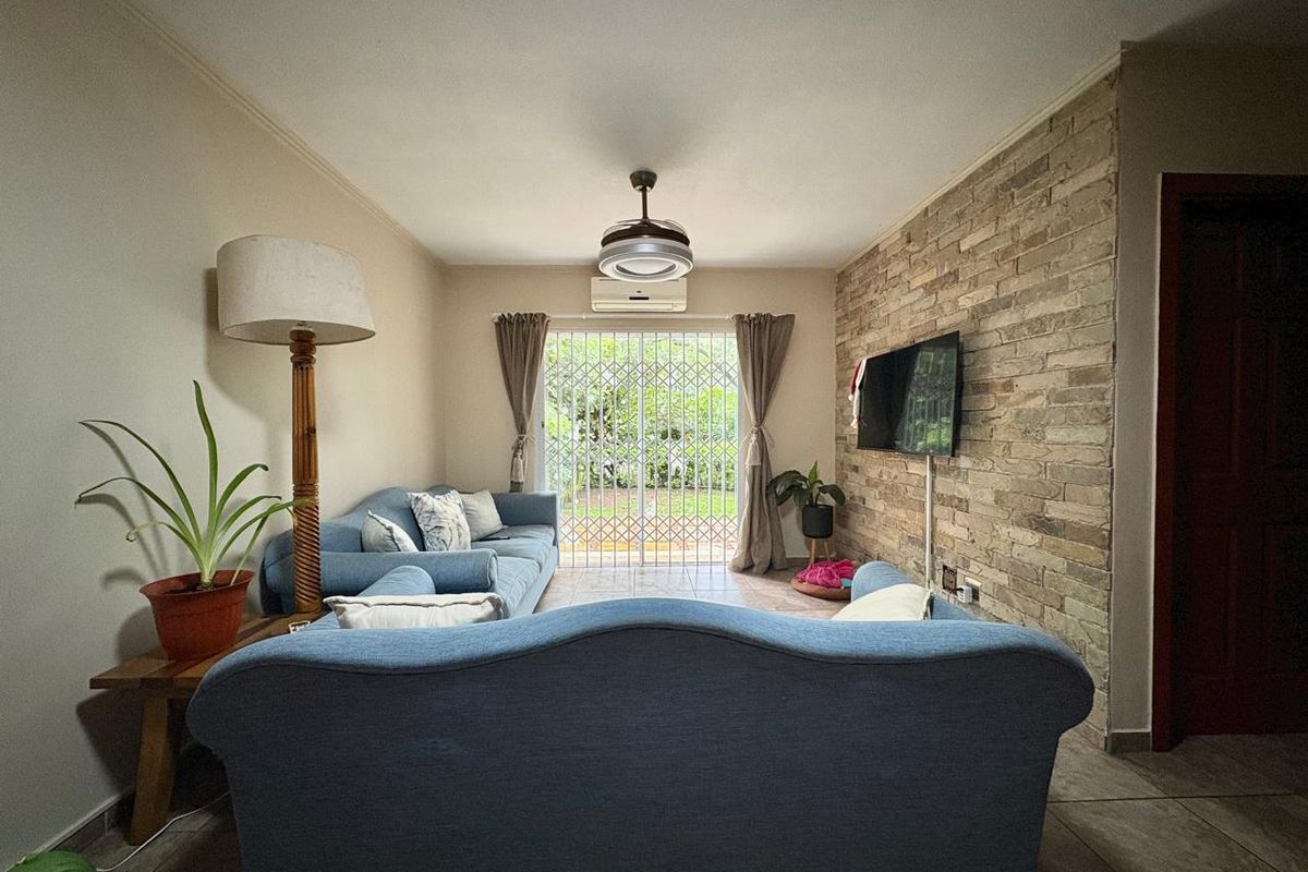A comfortable living room featuring a textured stone accent wall, tiled flooring, and direct access to the garden through a sliding glass door.