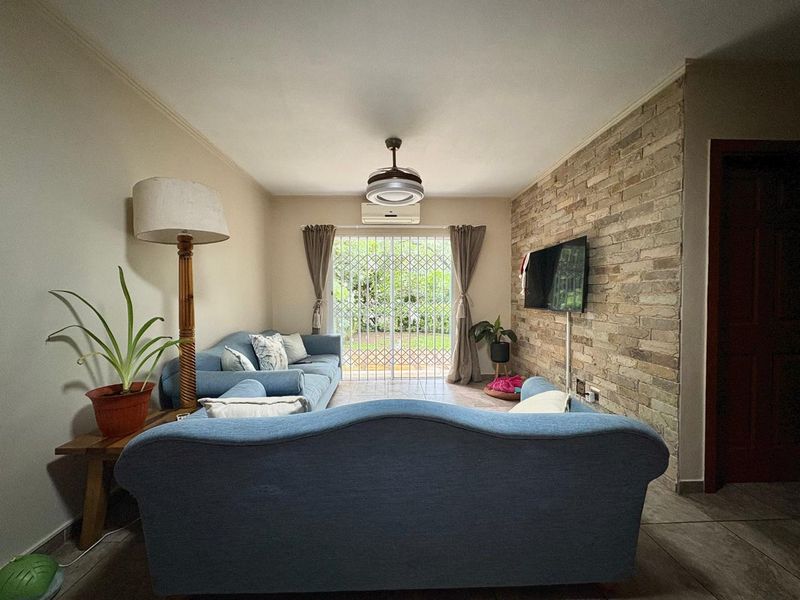 A comfortable living room featuring a textured stone accent wall, tiled flooring, and direct access to the garden through a sliding glass door.