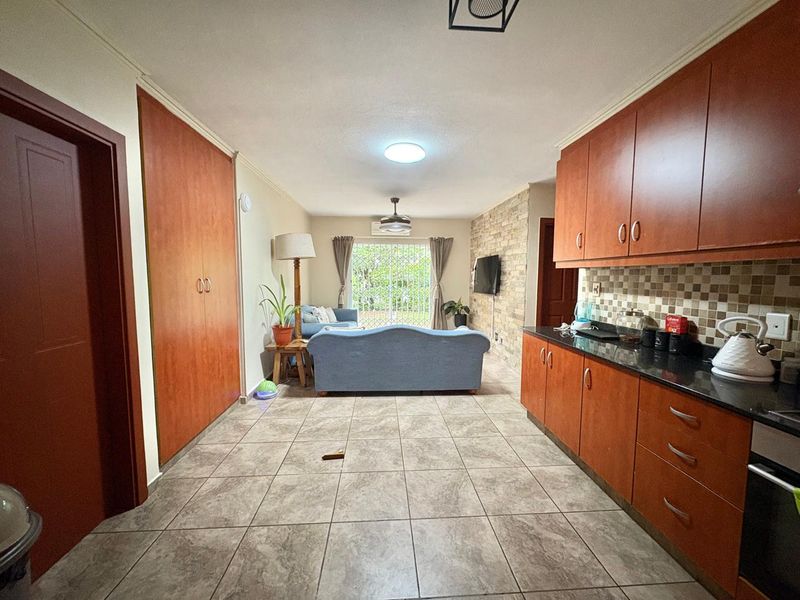 Open-plan living area featuring a kitchen with granite countertops and wood cabinetry, flowing into a lounge space with a stone feature wall and garden access.