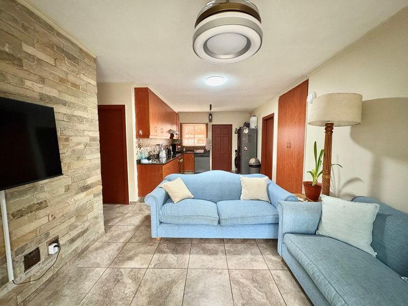Open-plan living area featuring a stone accent wall, tiled flooring, and a functional kitchen with wooden cabinetry and ample storage space.