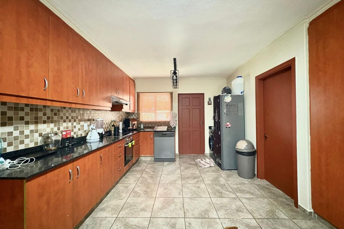 A functional kitchen featuring wood-finish cabinetry, granite countertops, a mosaic tile backsplash, and ceramic floor tiles, providing a practical workspace.