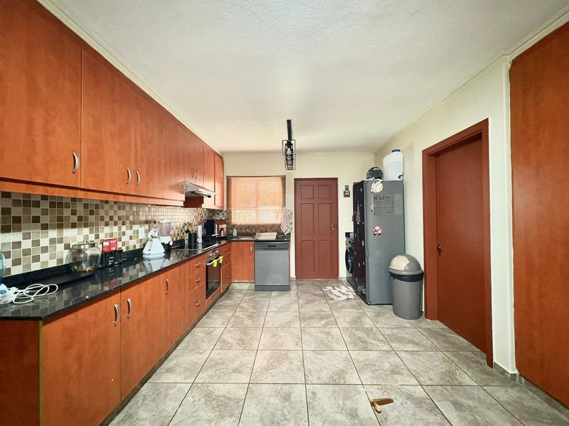 A functional kitchen featuring wood-finish cabinetry, granite countertops, a mosaic tile backsplash, and ceramic floor tiles, providing a practical workspace.