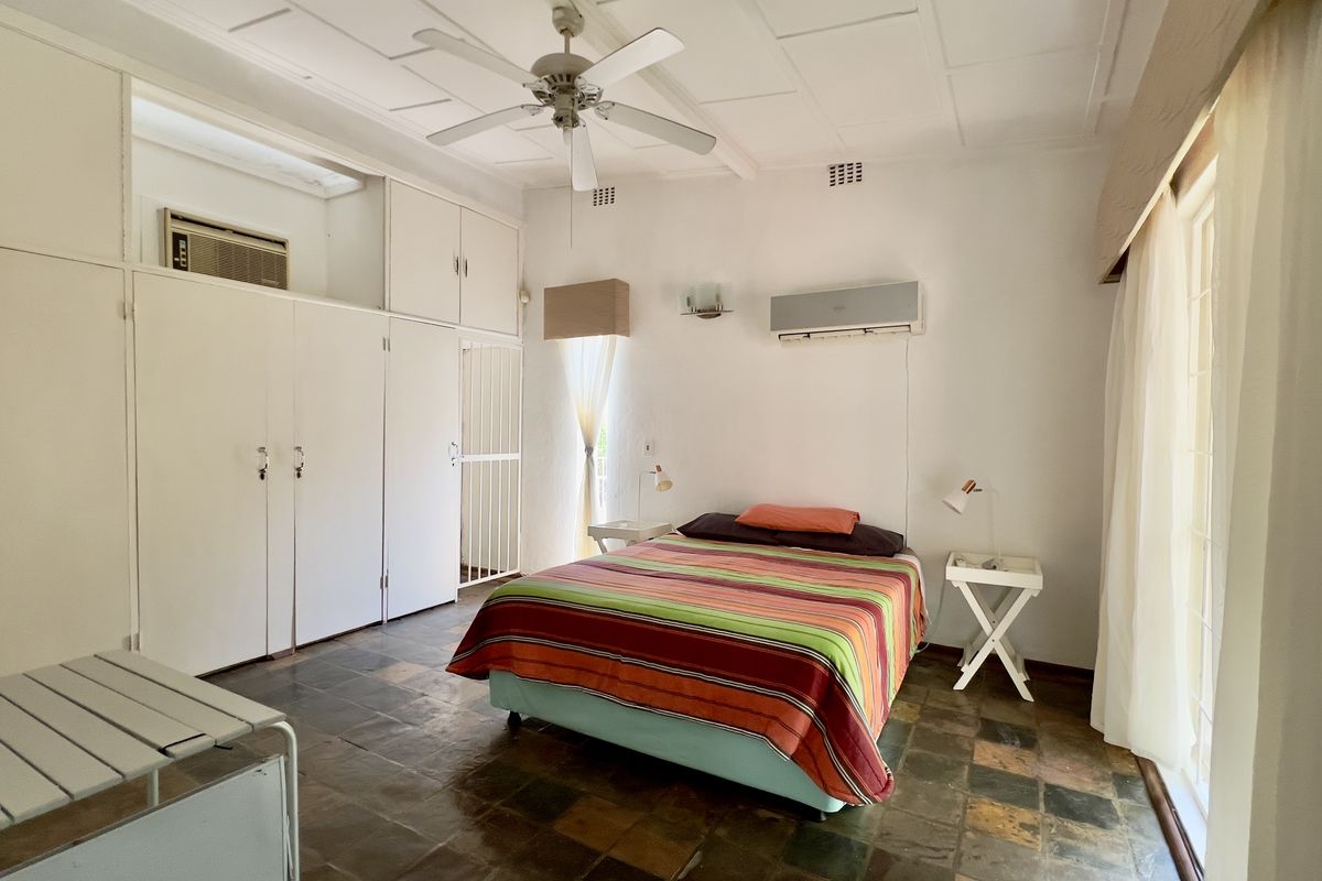 Spacious bedroom featuring slate tile flooring, extensive built-in cabinetry, a ceiling fan, and a wall-mounted air conditioning unit.