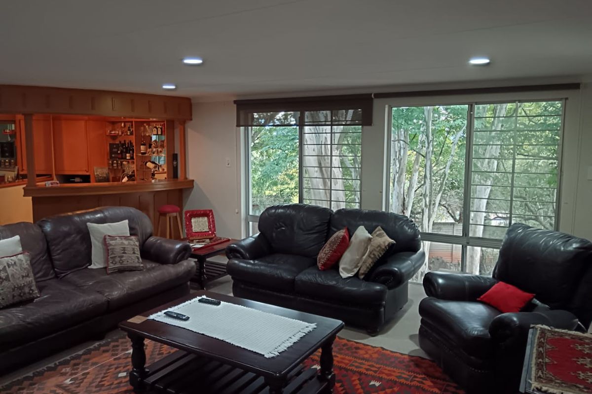 Spacious living room featuring a built-in wooden bar, recessed lighting, and large sliding glass doors with security bars overlooking the garden.