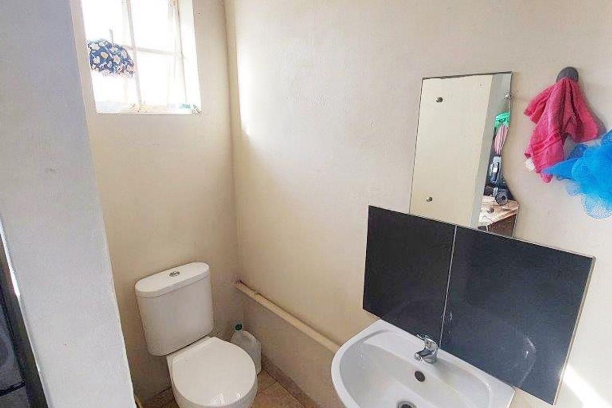 A compact bathroom featuring a pedestal basin, toilet, and tiled flooring, requiring cosmetic updates to improve its overall condition and aesthetic appeal.