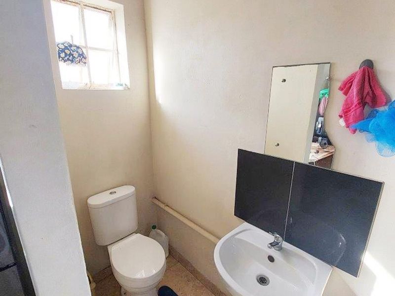 A compact bathroom featuring a pedestal basin, toilet, and tiled flooring, requiring cosmetic updates to improve its overall condition and aesthetic appeal.