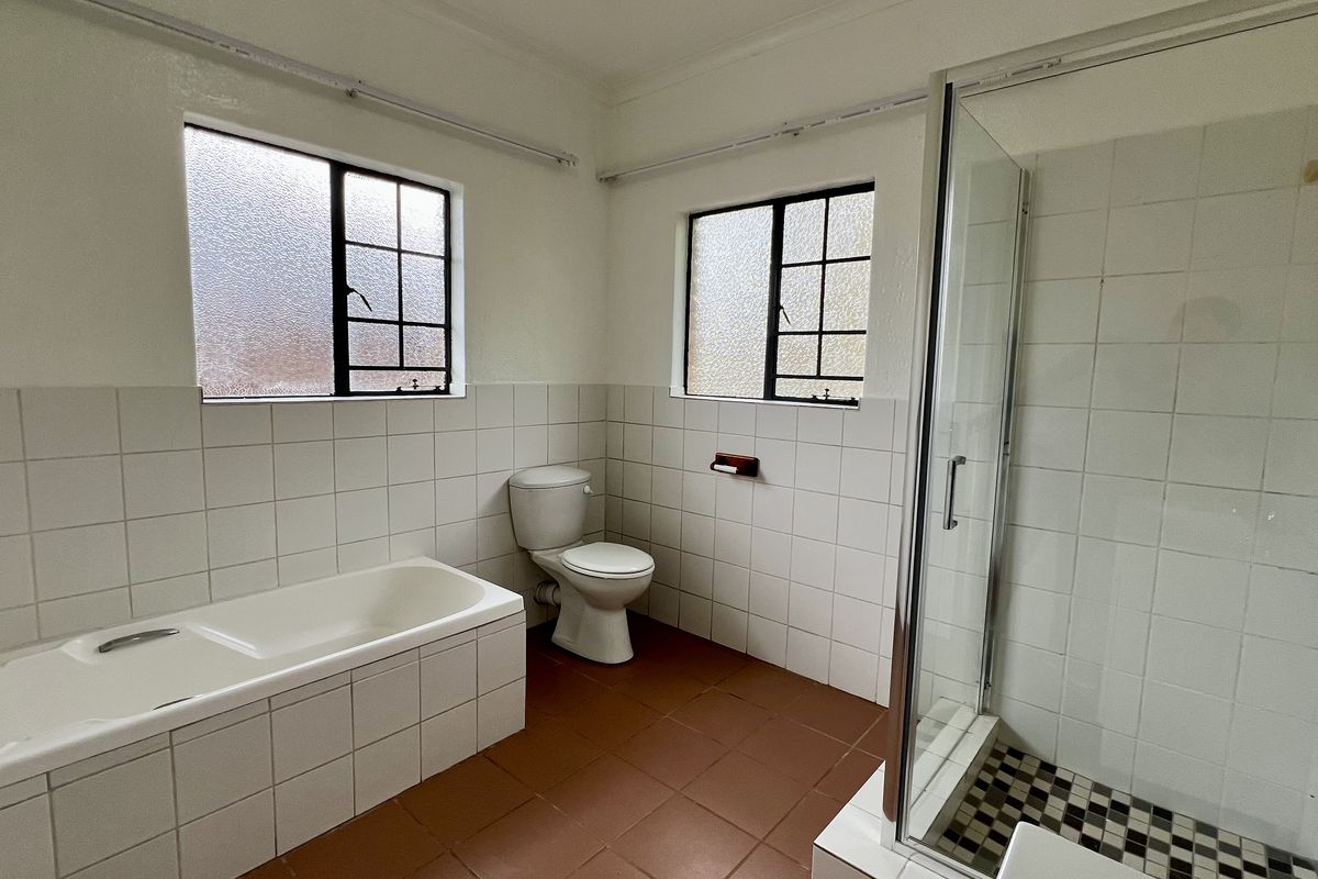 A spacious, empty bathroom featuring a built-in bathtub, separate shower enclosure, and toilet, finished with dated wall and floor tiling.