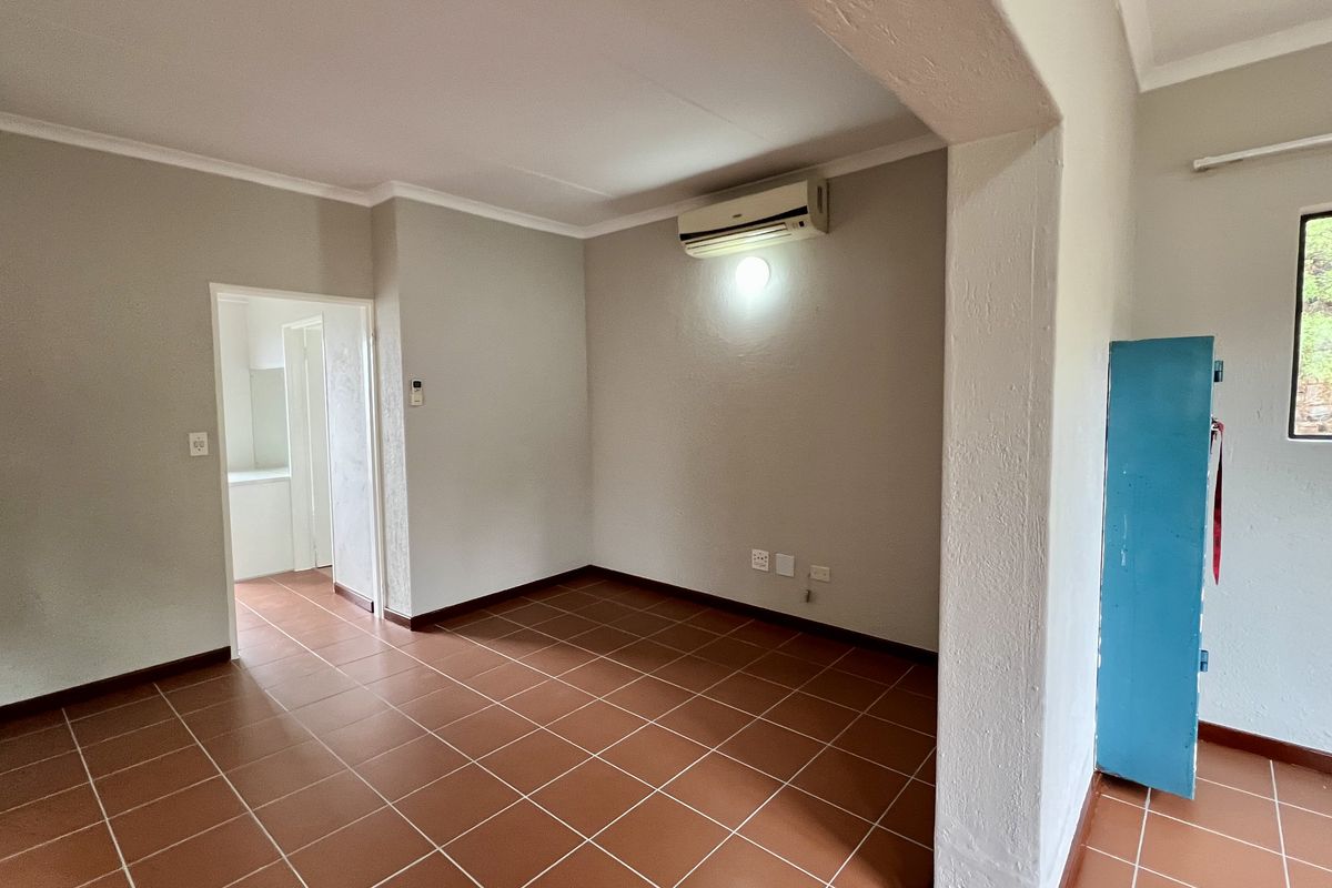 An empty living area featuring ceramic tile flooring, coved ceilings, and a wall-mounted air conditioning unit, with a doorway leading to an adjacent room.