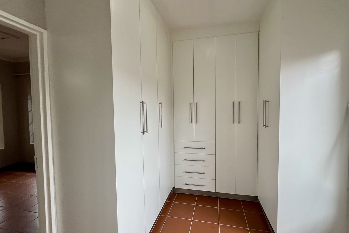 A clean, empty bedroom featuring white built-in cupboards with modern handles and terracotta-style tiled flooring.