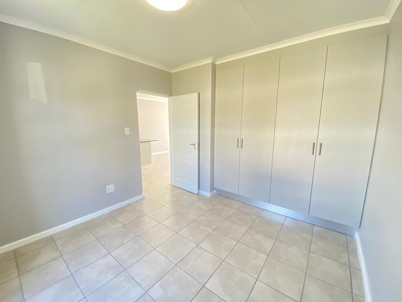 A clean, empty bedroom featuring neutral tiled flooring, built-in cupboards, and a coved ceiling, offering a bright and versatile living space.