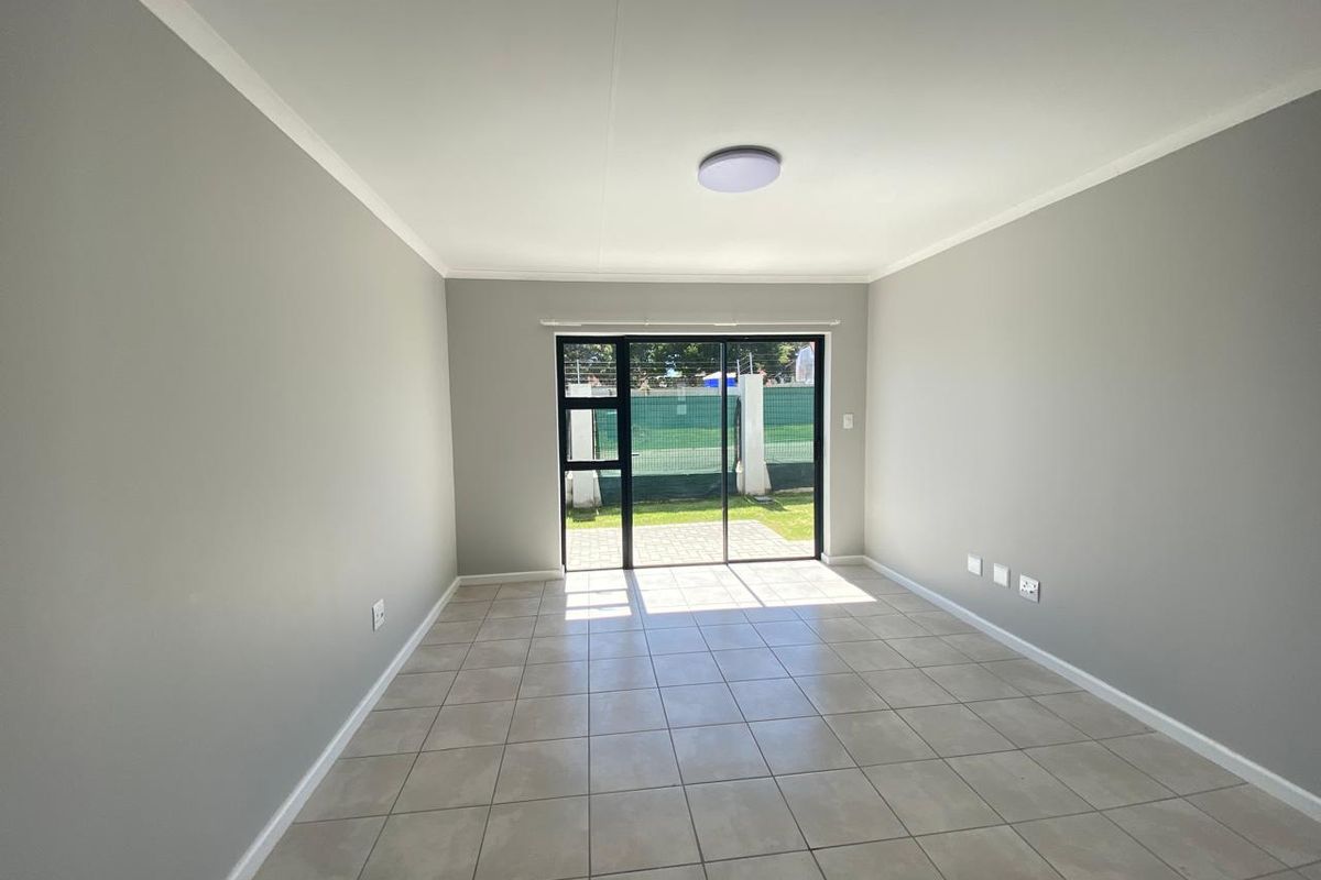 A bright, empty living room featuring neutral grey walls, tiled flooring, and a sliding glass door providing access to the outdoor area.