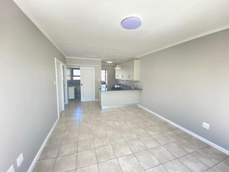 An open-plan living and kitchen area featuring neutral tiled flooring, modern cabinetry, and a functional kitchen island with a built-in hob.