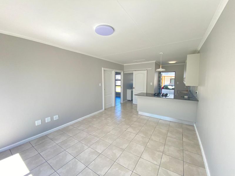 An open-plan living and kitchen area featuring neutral tiled flooring, modern cabinetry, a gas hob, and a functional kitchen island.