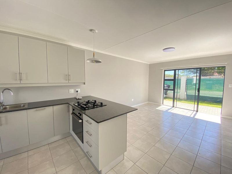 Modern open-plan kitchen and living area featuring neutral cabinetry, gas hob, tiled flooring, and direct access to the rear garden through sliding glass doors.