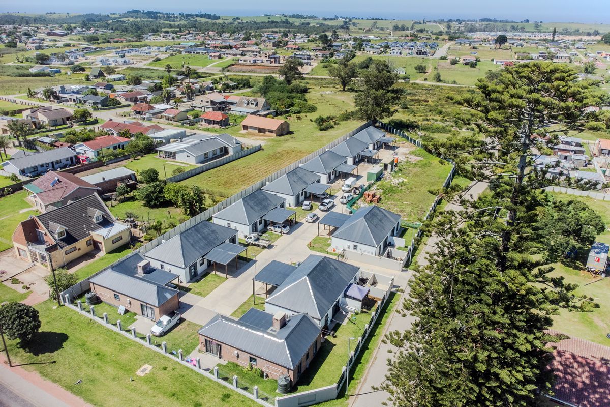 Aerial view of a residential complex featuring multiple detached units with paved driveways, carports, and perimeter walling in a suburban setting.