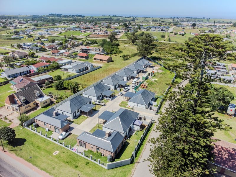 Aerial view of a residential complex featuring multiple detached units with paved driveways, carports, and perimeter walling in a suburban setting.
