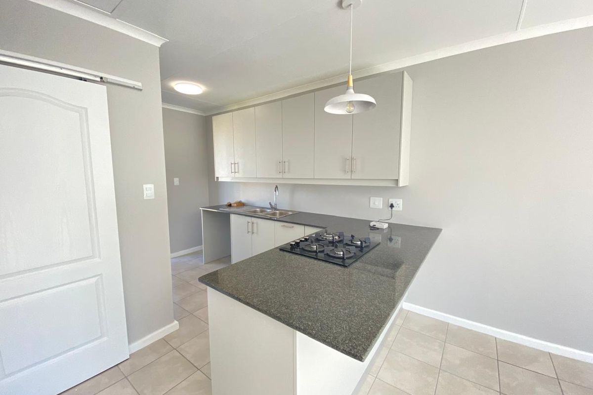 A clean, modern kitchen featuring neutral cabinetry, granite countertops, a built-in gas hob, and tiled flooring in an open-plan layout.