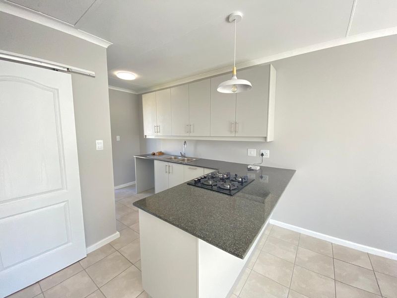 A clean, modern kitchen featuring neutral cabinetry, granite countertops, a built-in gas hob, and tiled flooring in an open-plan layout.