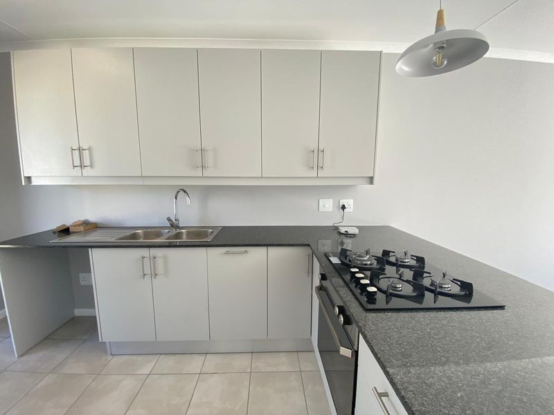 Modern kitchen featuring light grey cabinetry, dark granite countertops, a gas hob, built-in oven, and double sink with tiled flooring.