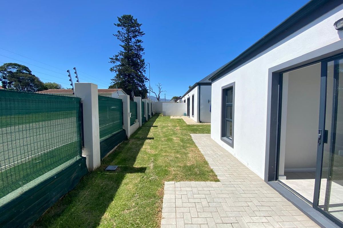 A well-maintained rear garden area featuring a paved walkway, manicured lawn, and secure boundary wall with electric fencing.