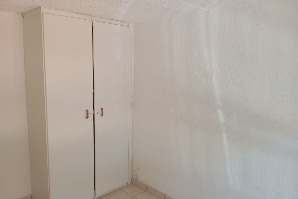 A simple bedroom featuring built-in white cabinetry and tiled flooring, offering a blank canvas for potential interior updates.
