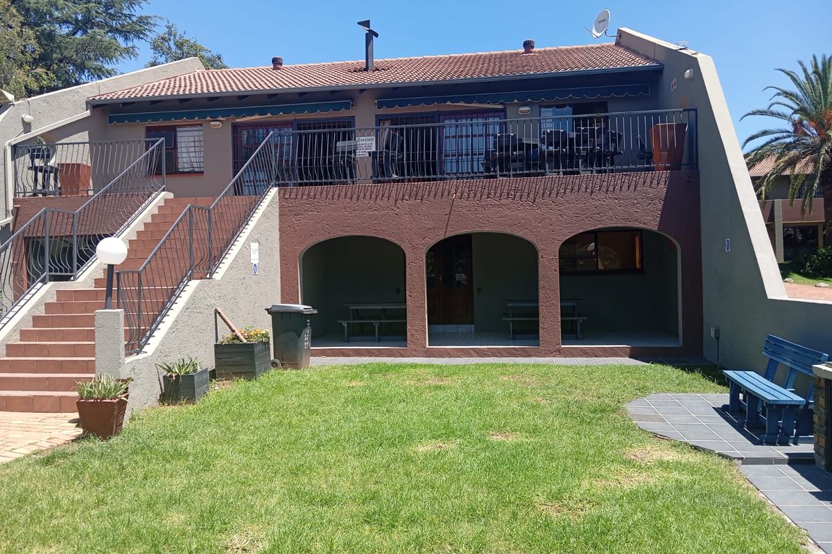 Rear view of the apartment building featuring a covered ground-floor patio, an elevated balcony with metal railings, and an external staircase leading to the upper level.