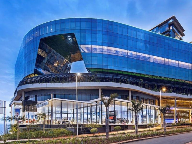 A striking modern multi-level commercial building featuring a prominent glass facade and contemporary architectural design, situated along a landscaped street.