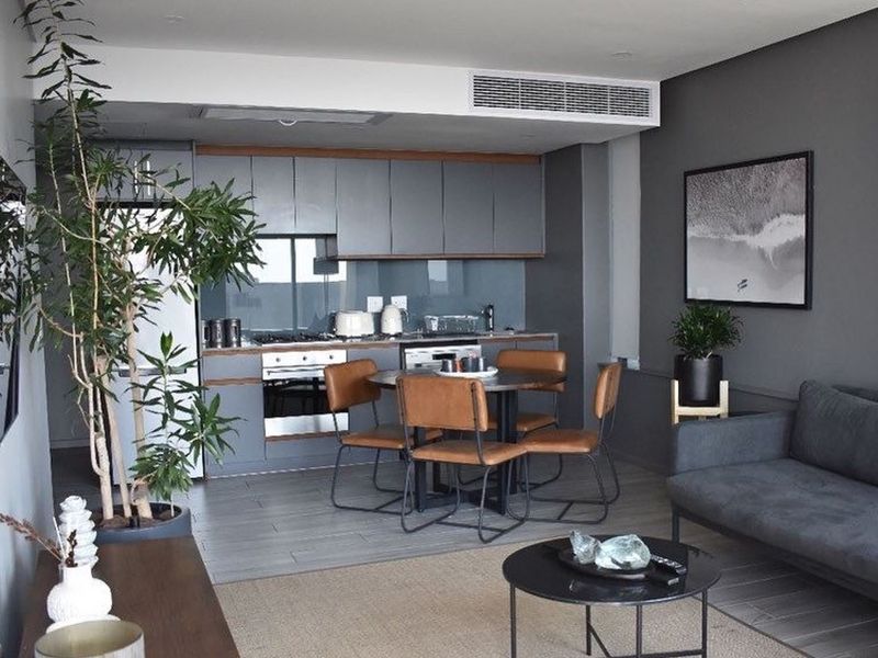 Modern open-plan living area featuring a sleek kitchen with built-in cabinetry, integrated appliances, and ducted air conditioning, finished with contemporary grey tones.