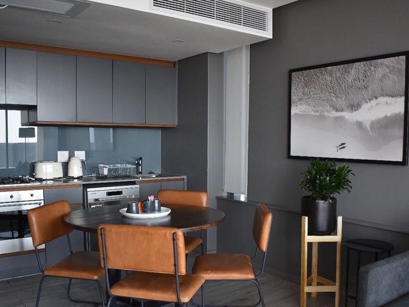 Modern open-plan kitchen featuring sleek grey cabinetry, integrated appliances, and a glass splashback, seamlessly flowing into the dining and living area.