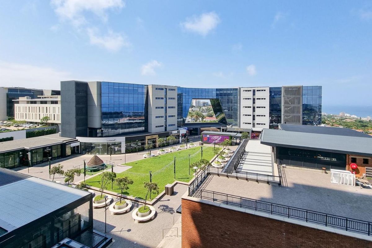 An elevated aerial view of a modern commercial complex featuring a central landscaped courtyard, glass-fronted buildings, and paved outdoor areas.