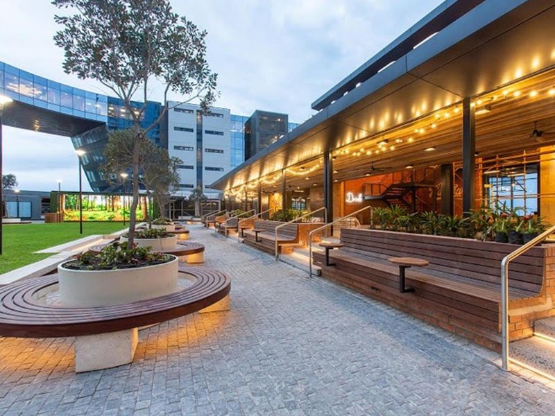 A modern, well-maintained outdoor patio area featuring integrated timber bench seating, cobblestone paving, and ambient LED lighting within a contemporary commercial complex.