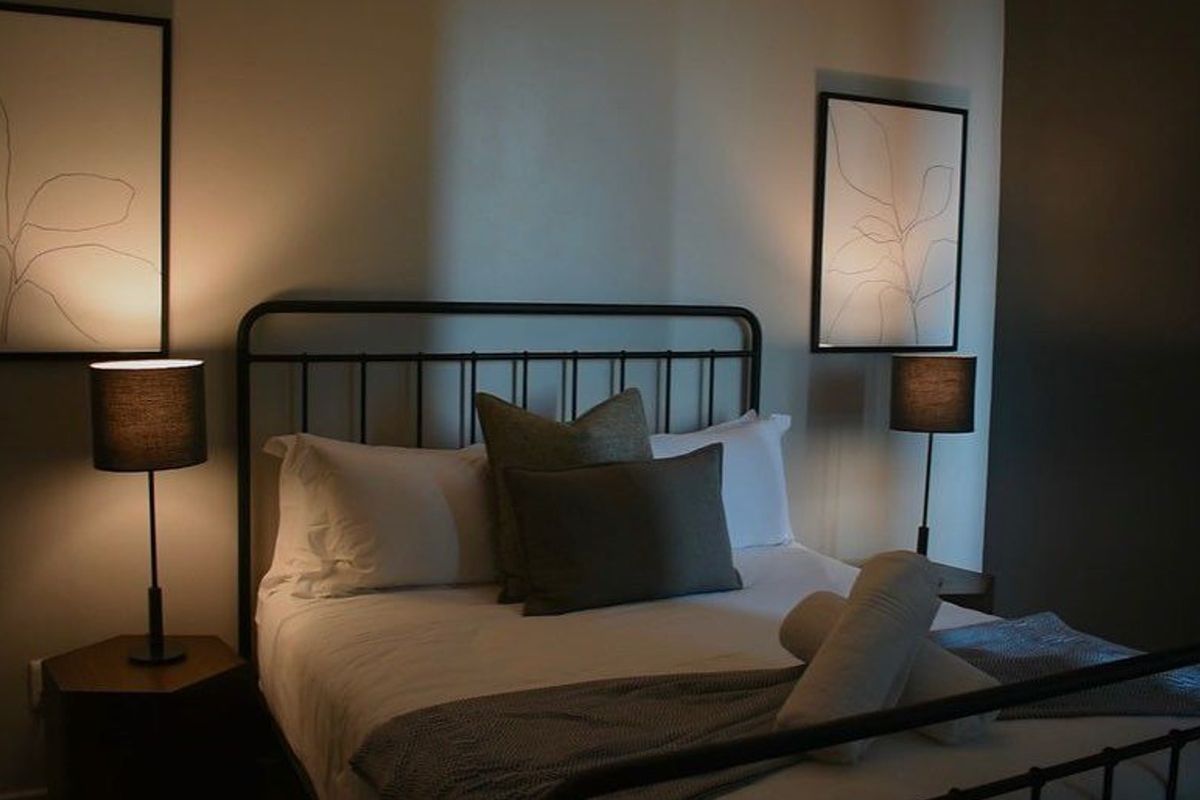 A cozy, dimly lit bedroom featuring a metal-framed bed and bedside lighting, creating a warm and inviting atmosphere.