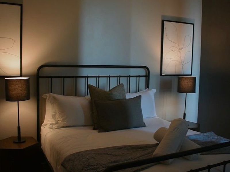 A cozy, dimly lit bedroom featuring a metal-framed bed and bedside lighting, creating a warm and inviting atmosphere.
