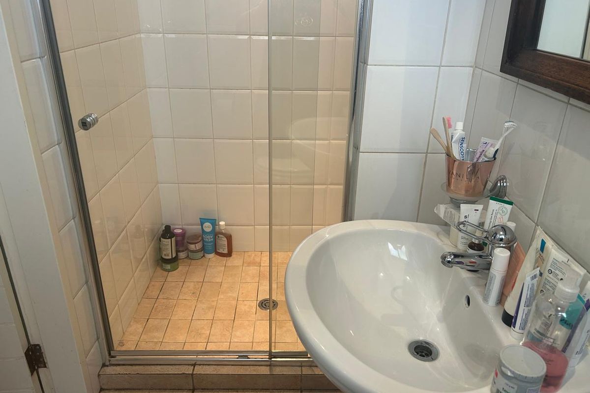 A functional bathroom featuring a glass-enclosed shower and a pedestal basin with chrome fixtures, finished with neutral ceramic wall and floor tiling.