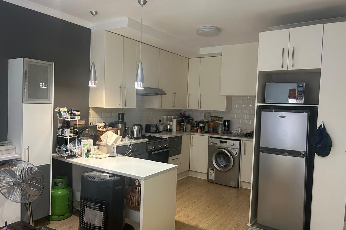 Compact kitchen featuring white cabinetry, subway tile backsplash, integrated oven, hob, and a breakfast bar with pendant lighting.