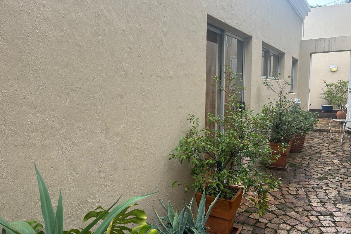 A rear exterior view of the apartment featuring a textured facade, sliding glass door access, and cobblestone paving.