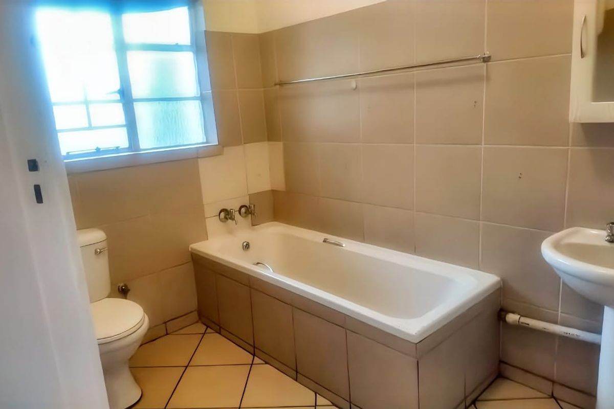 A dated bathroom featuring a standard bathtub, pedestal basin, and toilet with neutral wall and floor tiling.