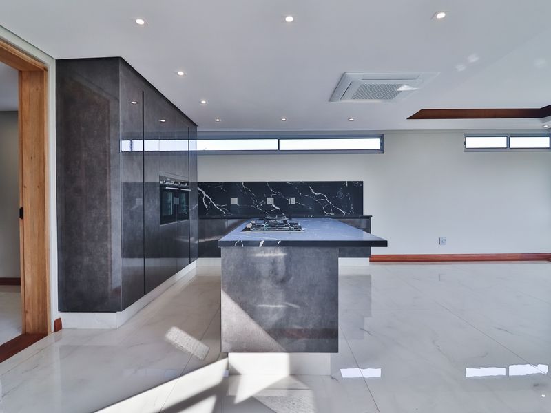 Modern open-plan kitchen featuring dark high-gloss cabinetry, a marble-look island with integrated gas hob, and sleek tiled flooring.
