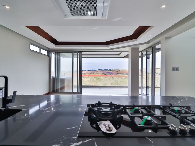Modern open-plan kitchen featuring a sleek black marble island with a built-in gas hob, recessed ceiling lighting, and expansive sliding doors opening to scenic views.
