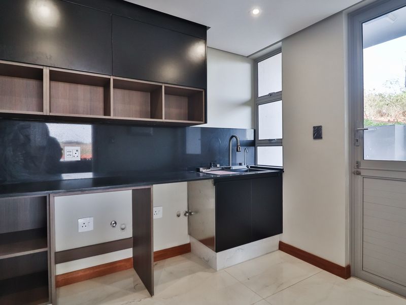 Modern scullery featuring sleek dark cabinetry, stone countertops, integrated sink, and direct access to the exterior.