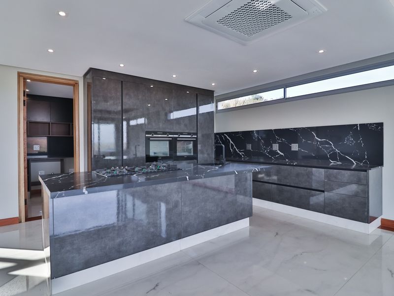 Modern kitchen featuring high-gloss cabinetry, marble-look countertops, integrated oven and hob, and a convenient adjoining scullery area.
